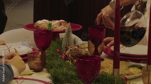 Christmas dinner table with red glasses, bolo rei cake, and wine being poured