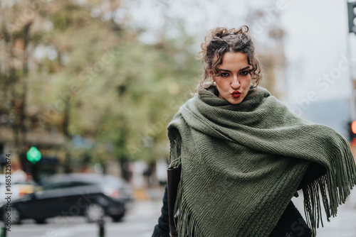 Fotografie A stylish young woman wrapped in a green shawl strikes a playful pose outdoors in an urban environment, blending perfectly with the vibrant city backdrop and exuding a confident and cheerful vibe