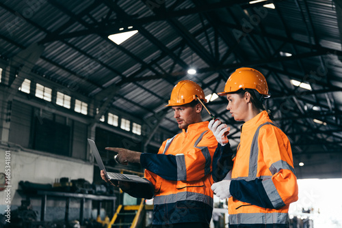 Quadro em tela Two engineers wearing safety helmets and orange reflective jackets discuss industrial operate checking train maintenance at station, representing teamwork, safety and transportation and teamwork