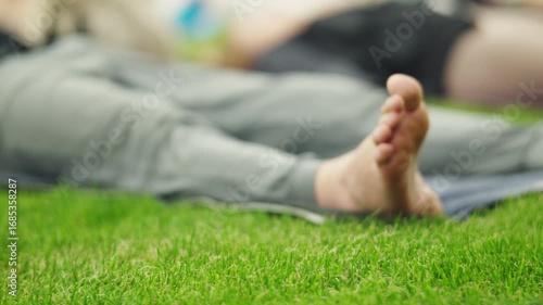 Dozens of people relax on mats in a green field after a group FYSM yoga class, enjoying the peaceful aftermath of their practice.