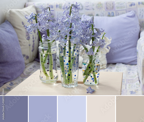 Color palette swatches of violet hyacinth flower in glass vase on light wooden table and beige purple pillows background. Pastel trendy combination. Fresh colorful natural inspiration for styling.