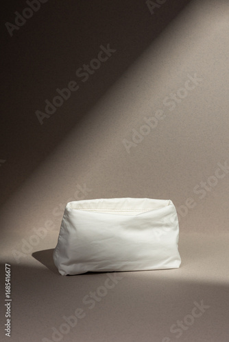 Minimalist photo of a white fabric pouch placed under dramatic lighting on a neutral background. Perfect for themes of fashion, cosmetics, lifestyle, branding mockups, and product presentation.