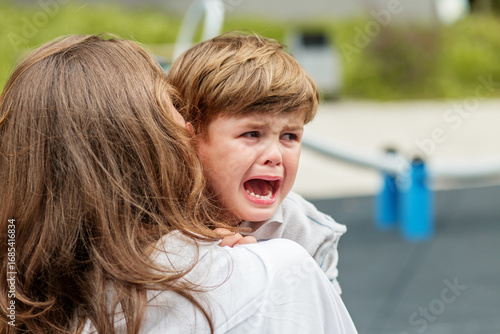 Crying child being comforted by mother outdoors