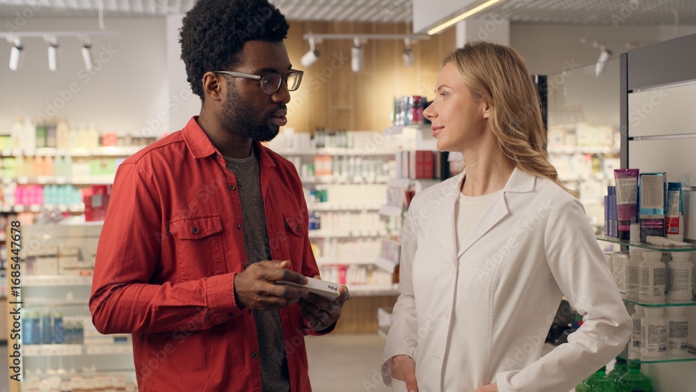 Obraz premium Multiracial woman man in pharmacy medical consultation pills dosage help African American customer Caucasian pharmacist doctor in coat conversation medicine buying healthy medication vitamins advice