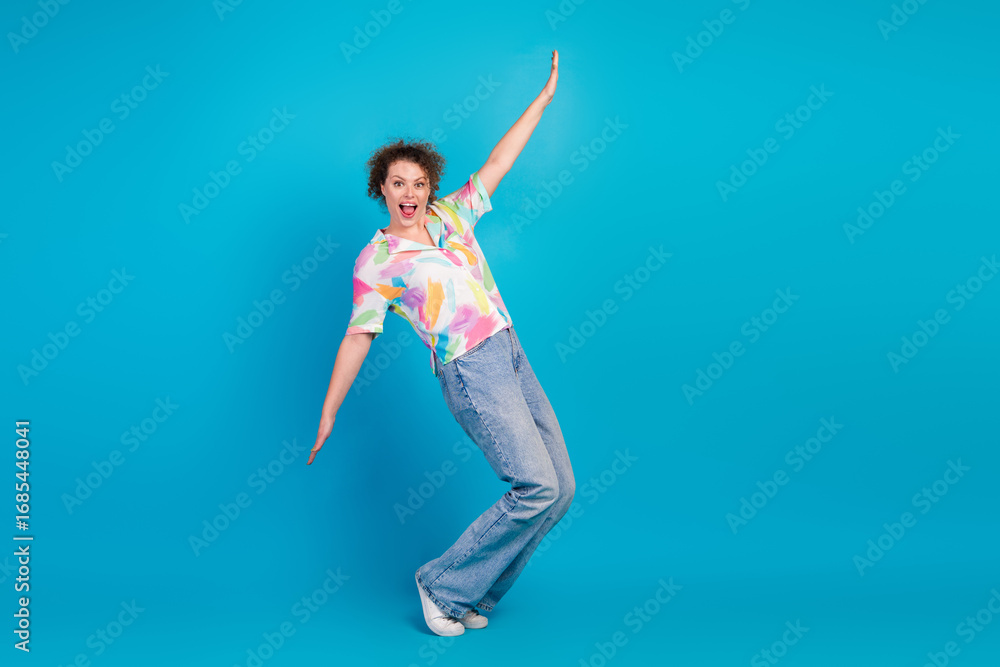 Obraz premium Happy young woman in stylish outfit posing joyfully against a bright blue background, embracing fun and energy