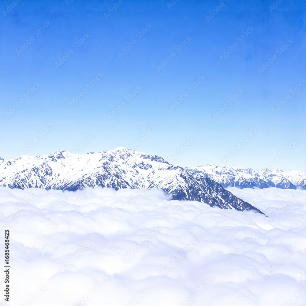 Fototapeta premium Snowy Mountain Peaks Above Clouds Against a Clear Blue Sky