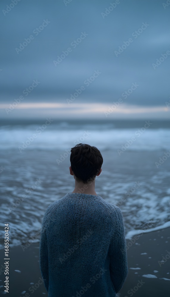 Fototapeta premium A lone man in a wool sweater stands by the ocean at twilight