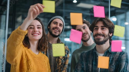 Collaborative brainstorming session with diverse young professionals using sticky notes on glass wall.