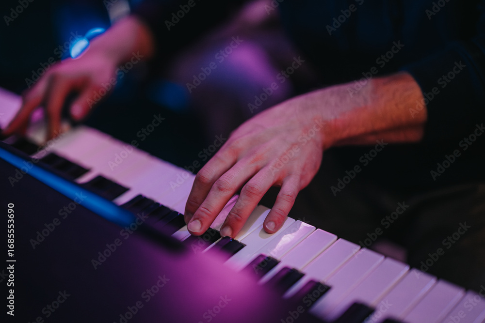 Obraz premium A detailed view of a person's hands gracefully playing the piano in a dimly lit room, conveying emotion and expertise. The ambient lighting adds drama and focus to the musical performance.