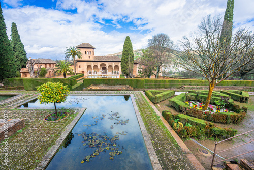A stunning view of the Partal Gardens within the historic Alhambra complex. The serene pond, lush hedges, and beautiful Nasrid architecture create a perfect image.