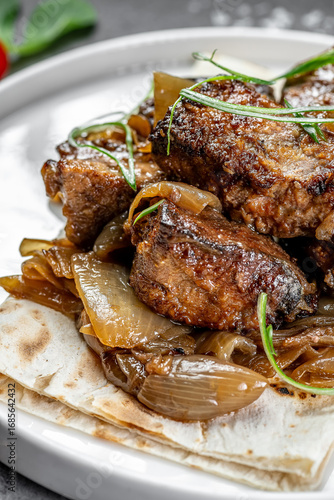 Savory beef dish with caramelized onions. Tender beef pieces served over slow-cooked caramelized onions on a plate, garnished with herbs.