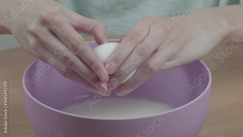 Close-up of woman cracking a chicken egg over a bowl of kefir for dough preparation in her kitchen, recorded with ambient sound.