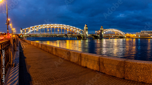 Night panorama of illuminated Bolsheokhtinsky Bridge with reflection in Neva River and granite embankment. Saint Petersburg, Russia.