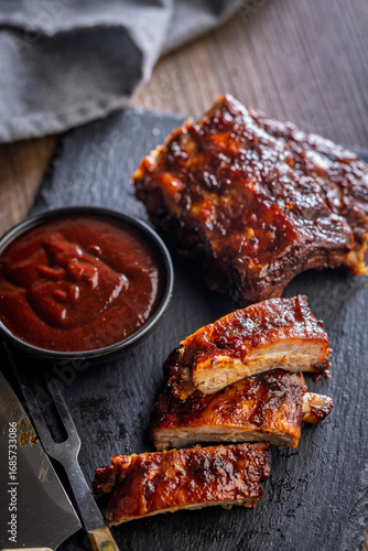 Pork BBQ glazed ribs and sauce on black table.