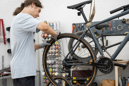 A bicycle mechanic repairs the rear wheel of a bike in a well-lit workshop, focusing on the brake system while wearing gloves for protection and cleanliness.
