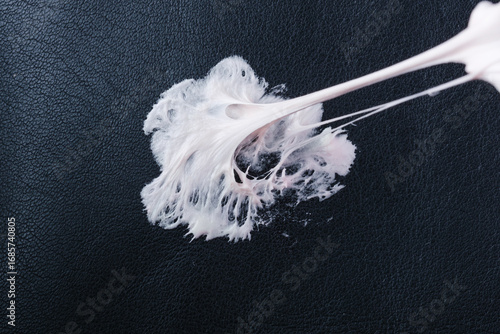 Chewing gum has become stuck on a black leather textured surface, showing its stretching and gooey consistency. Concept of daily stains. Spot-cleaning sticky mess upholstery seating. top view. 
