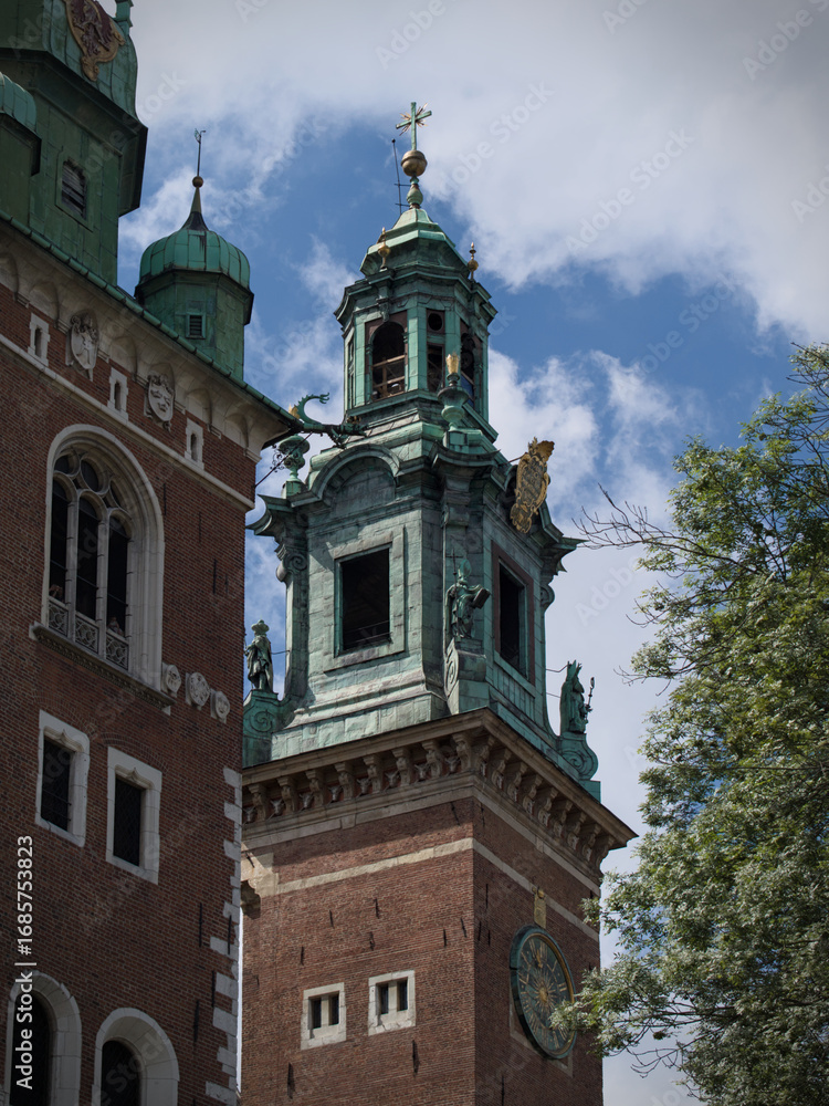 Obraz premium Historic church tower with a green copper roof and a sundial, set against a cloudy blue sky.