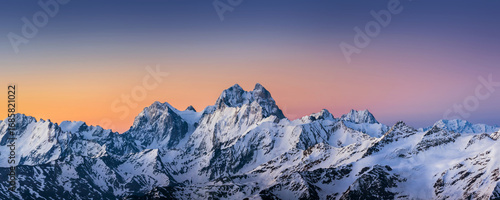 Panoramic view of the Ushba and Skhelda peaks at sunrise under the clolrful sky. Steep rocky caucasian mountains, a part of the Main Caucasian range, in winter sunny morning.