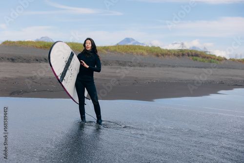 Happy surfer woman in wetsuit with surfboard go to winter surfing in ocean. Adventure Extreme travel sport concept