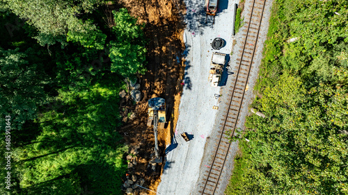 Obraz na plátně Construction workers and machinery are present by the railway tracks, clearing land surrounded by green foliage