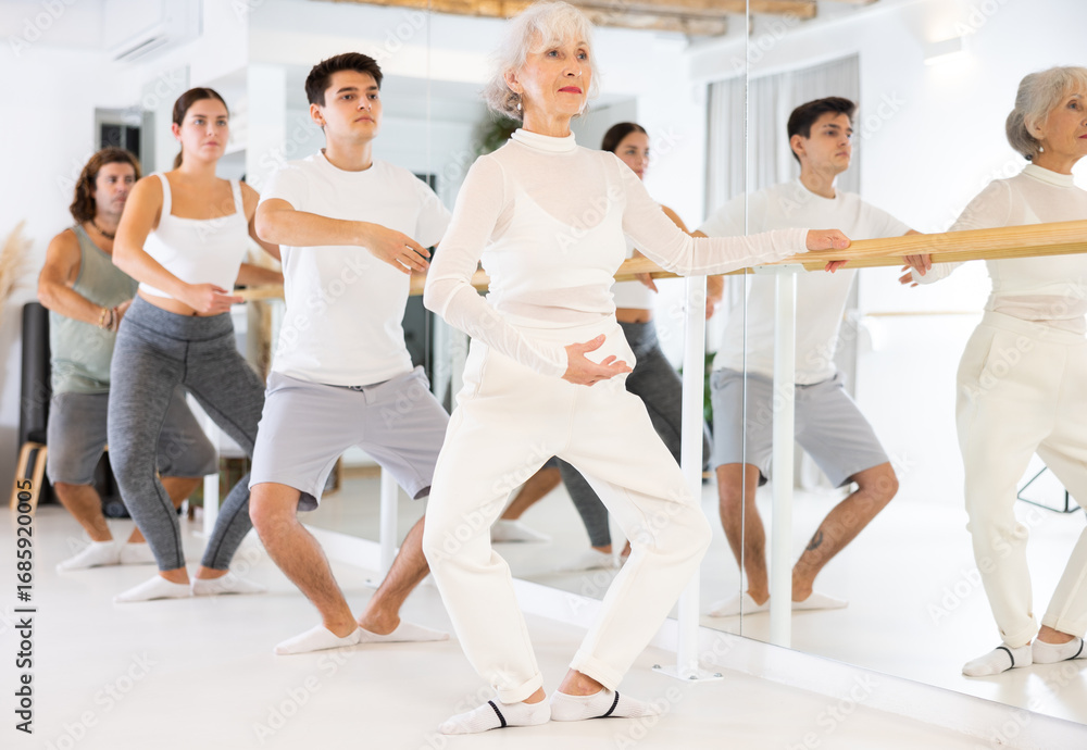 Naklejka premium Slender elderly woman doing choreography at ballet barre during gym classes