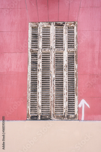 old wooden shutters on a red wall with peeling paint, symbol of time and decay. minimal urban detail with arrow graffiti pointing upwards, street photography