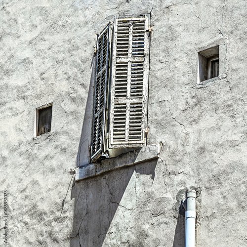 Old weathered shutter on textured white wall, Marseille, France. Mediterranean urban detail with shadow and patina, minimal architecture