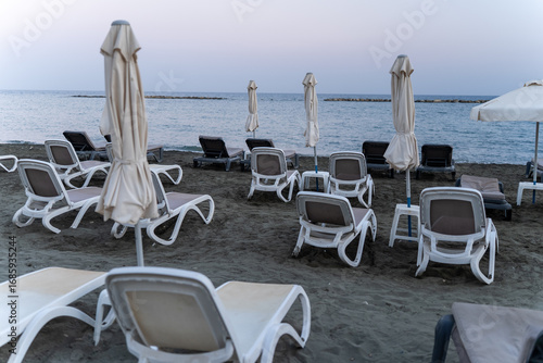 Beach in Limassol, Cyprus, with white sunbeds and umbrellas by the sea. Morning scene on the Mediterranean seaside promenade.
