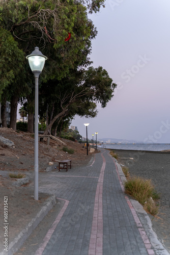 Pedestrian walkway with street lamps by the sea on the Limassol promenade in Cyprus. Evening view of the Mediterranean coastline.
