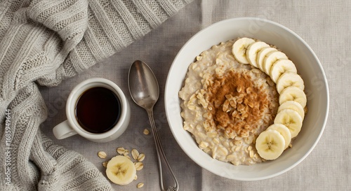 Cozy breakfast setting featuring oatmeal with banana, cup of dark beverage and a cozy sweater on a linen cloth.