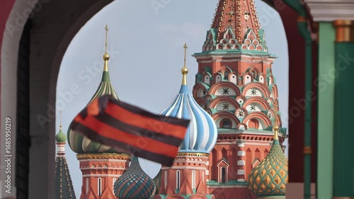 Saint Basil's Cathedral framed by Resurrection Gate with waving Ribbon of Saint George in Moscow.