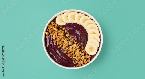 Delicious acai bowl with fresh bananas and granola, presented on a vibrant turquoise background.