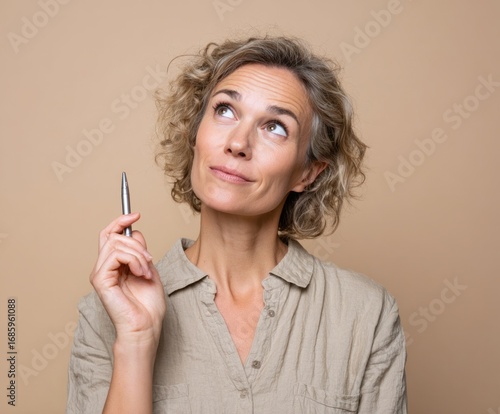 Thoughtful woman in a light beige blouse contemplates a creative idea, holding a metallic pen aloft.
