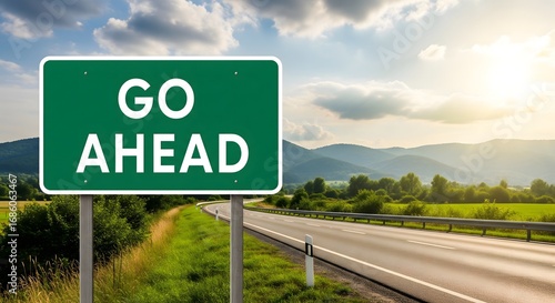 Green road sign with text Go Ahead on highway with scenic mountains and sunlight, symbolizing motivation, progress, future journey, success, opportunity, and positive direction