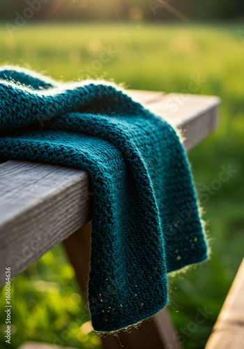 Teal knitted blanket draped gracefully over a weathered wooden bench in a sun-drenched outdoor setting creating a cozy and inviting scene