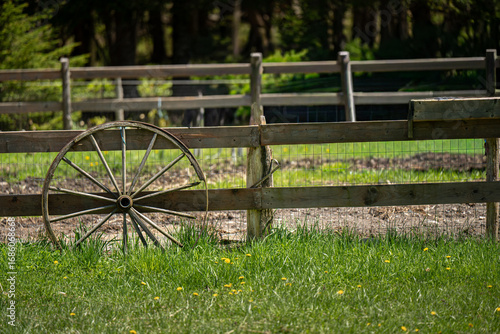 old cart wheel leaning against an old rustic fence on horse ranch.