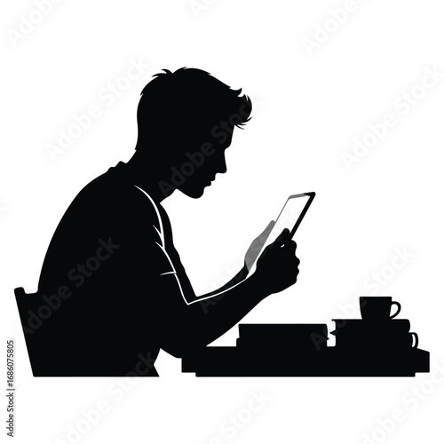 Silhouette of a young man sitting at a desk using a tablet device.