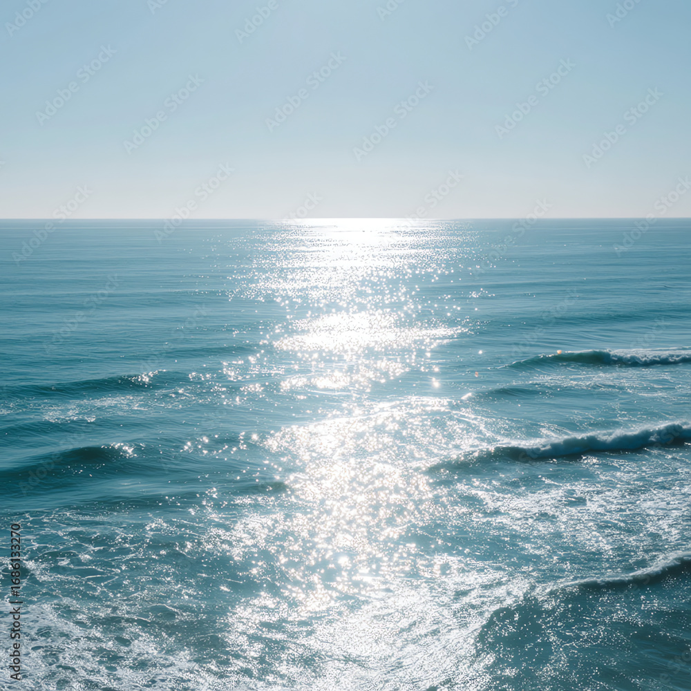 Fototapeta premium Sunlight sparkles on calm ocean waves under a clear blue sky, creating a serene and peaceful seascape with gentle ripples and shimmering reflections