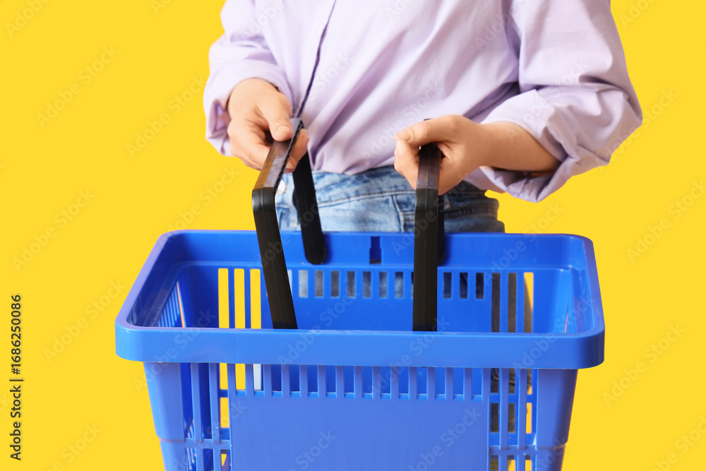 Fototapeta premium Woman with blue shopping basket on yellow background