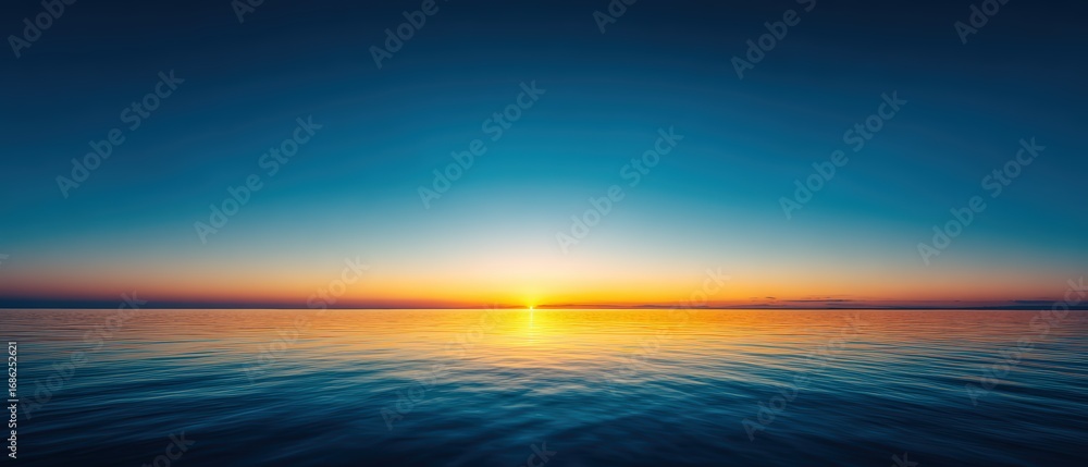 Obraz premium Stunning ocean sunset with vibrant orange and yellow hues over calm water and clear blue sky creating a tranquil natural scene