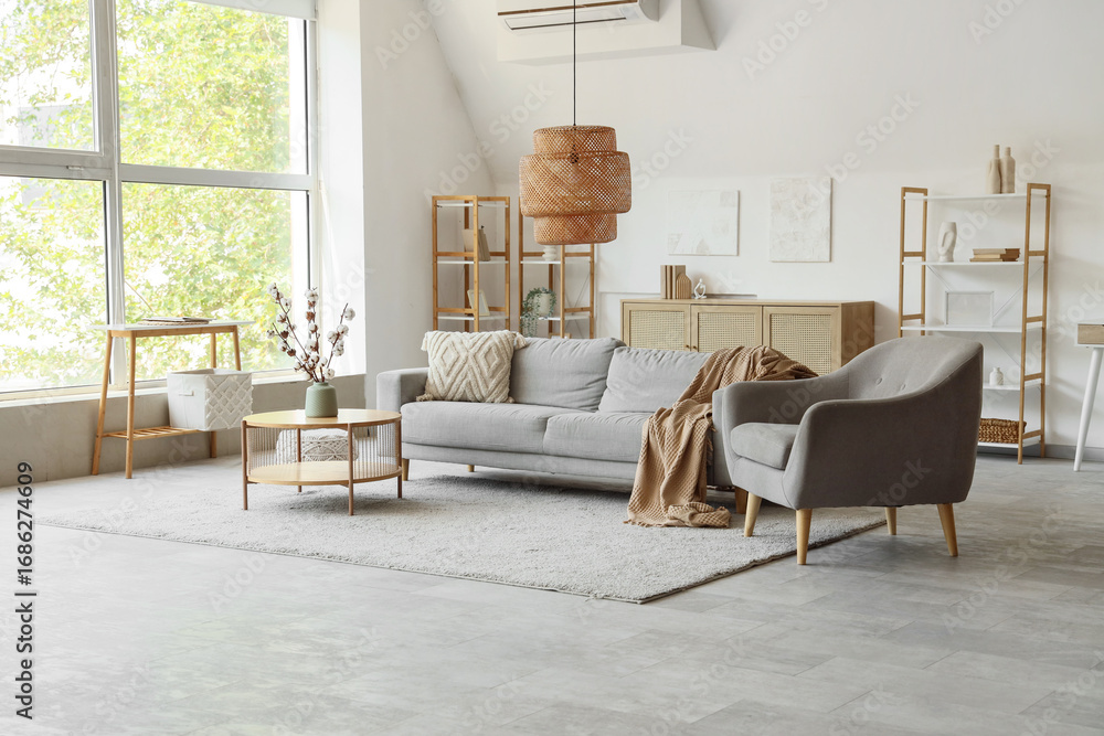 Fototapeta premium Modern living room interior with gray sofa, armchair, and wooden furniture by a large window