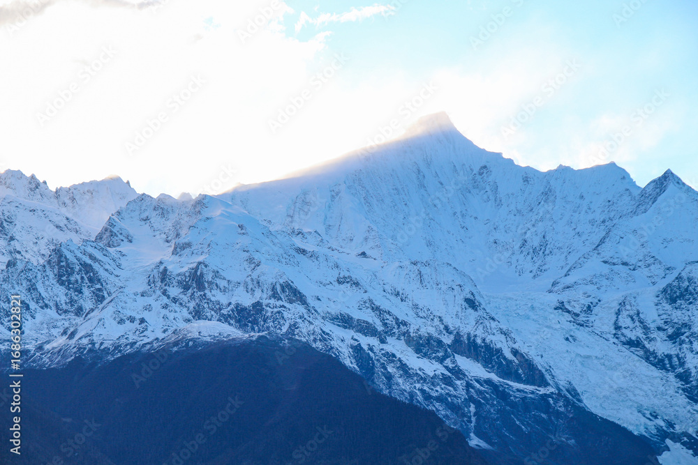 Fototapeta premium Jagged, snowy peaks loom under a cloudy sky Yala Snow Mountain, Sichuan, China