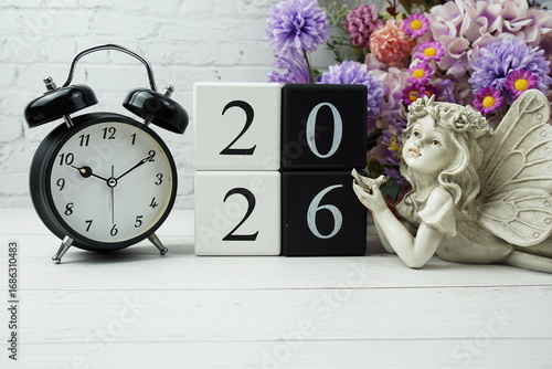 Happy New Year 2026 with wood block number on wooden table background decorations with alarm clock flowers bouquet and angel statues home decorations