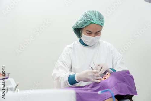 Asianfemaledentist conducting teeth inspection using dental explorer on adult female patient in dental chair during oral examination procedure at clean clinic with purple covering cloth