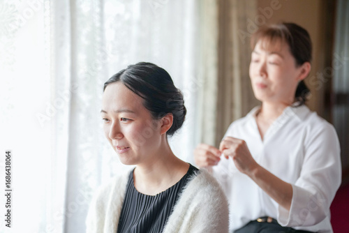 Free Download A woman is sitting in front of a window while another woman is braiding her hair. The woman getting her hair braided has a sad expression on her face - GFXLoad