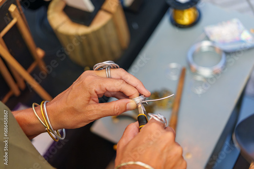 Murais de parede Metalsmith bending aluminum wire, creating intricate handcrafted jewelry beside