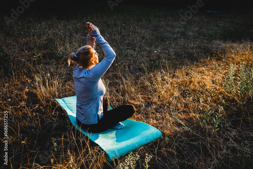 Obraz na plátne Woman practicing yoga and meditation on nature sitting in lotus pose on yoga mat, relaxed with closed eyes