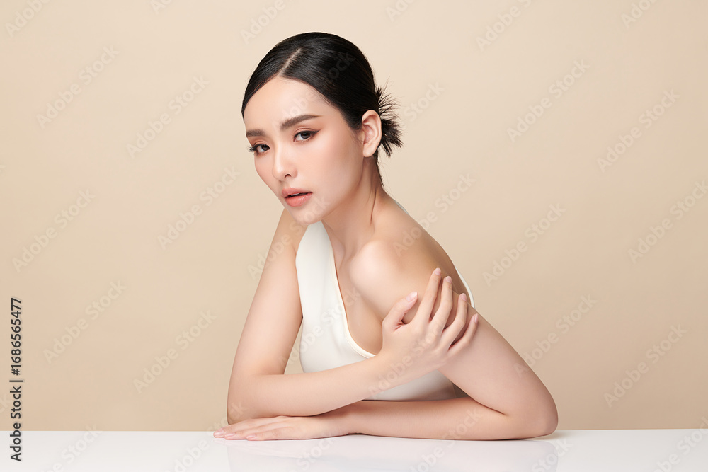 Fototapeta premium A beautiful young Asian woman with clean, fresh skin against a beige background. Skincare, facial treatment, cosmetology, beauty, and spa. An elegant portrait of an Asian woman.
