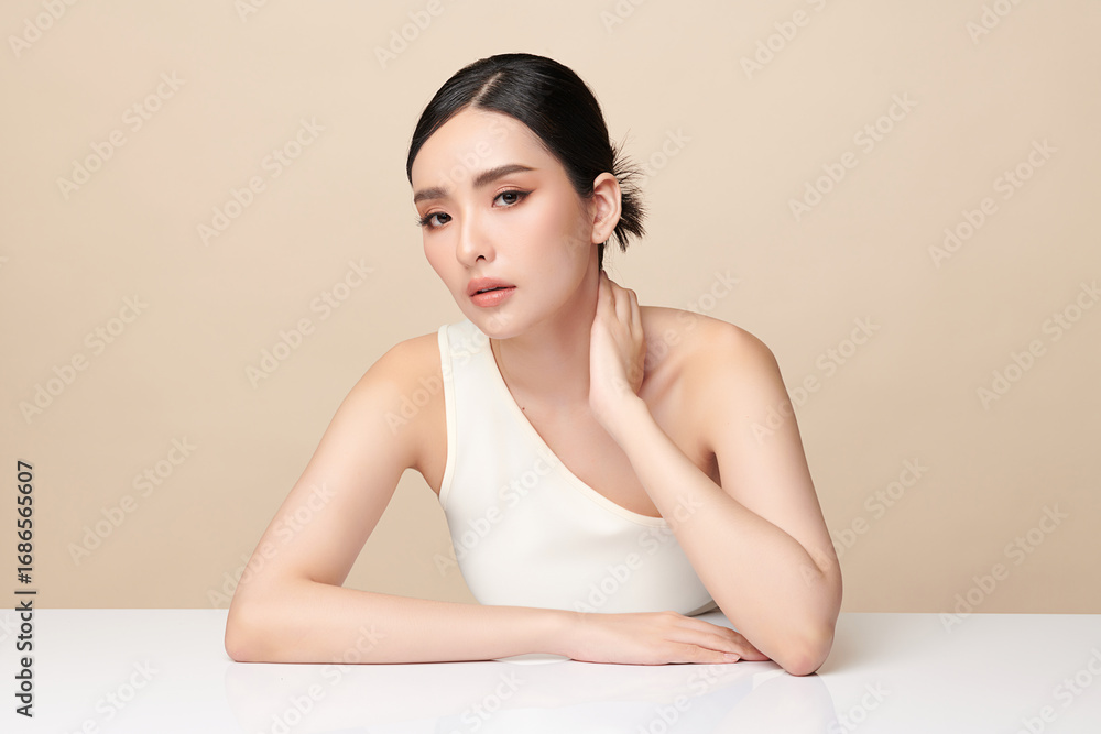 Fototapeta premium A beautiful young Asian woman with clean, fresh skin against a beige background. Skincare, facial treatment, cosmetology, beauty, and spa. An elegant portrait of an Asian woman.