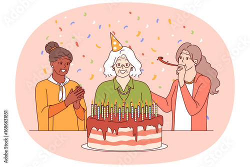 Birthday of elderly woman standing near large cake with candles and happy friends. Confetti around elderly people celebrating birthday and using whistle to create cheerful festive atmosphere